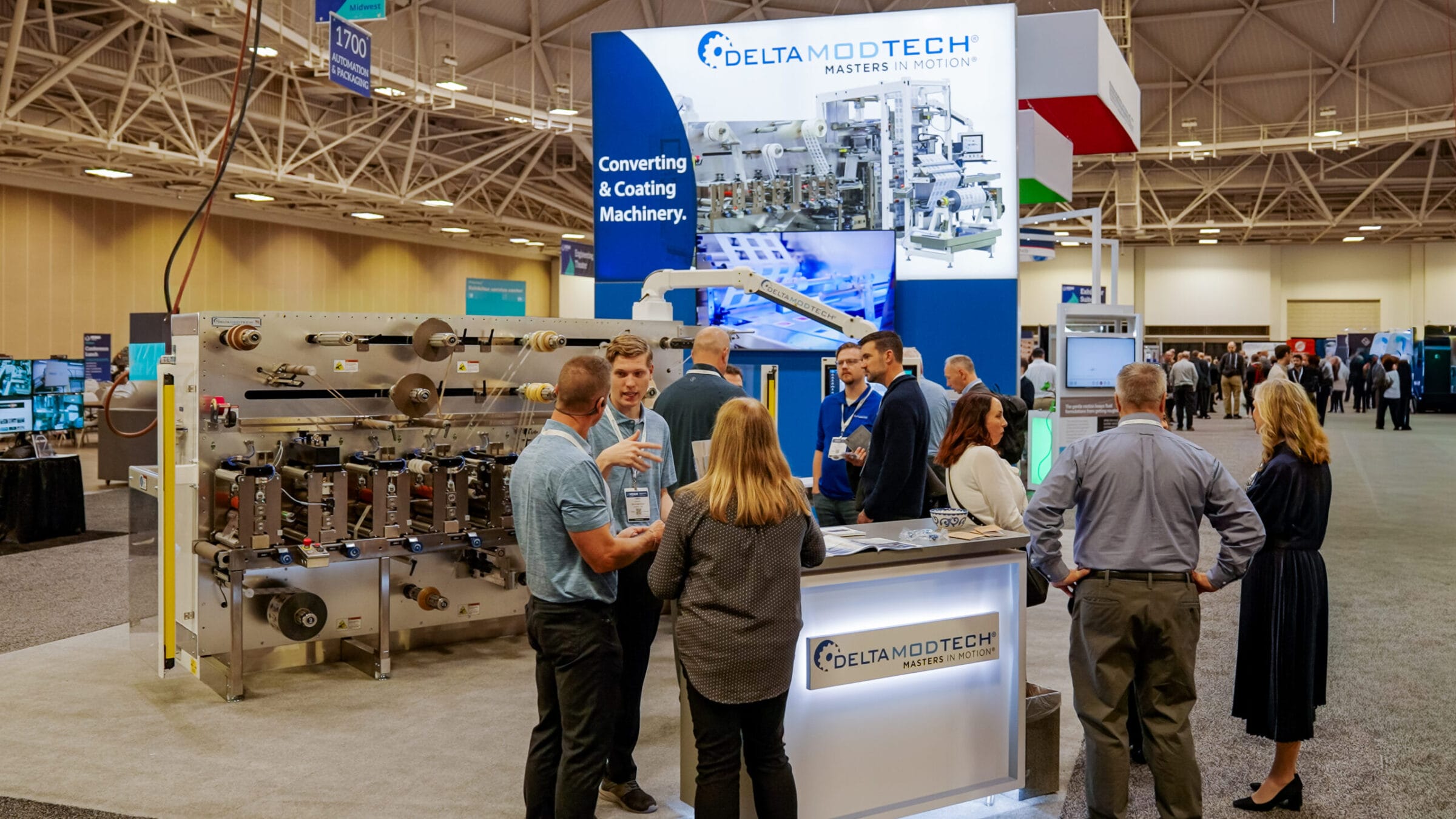 People gathered around Delta ModTech converting and coating machinery at a trade show.