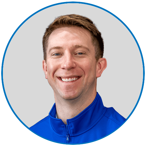 Man with short brown hair and blue eyes, smiling, wearing a blue zip-up jacket.