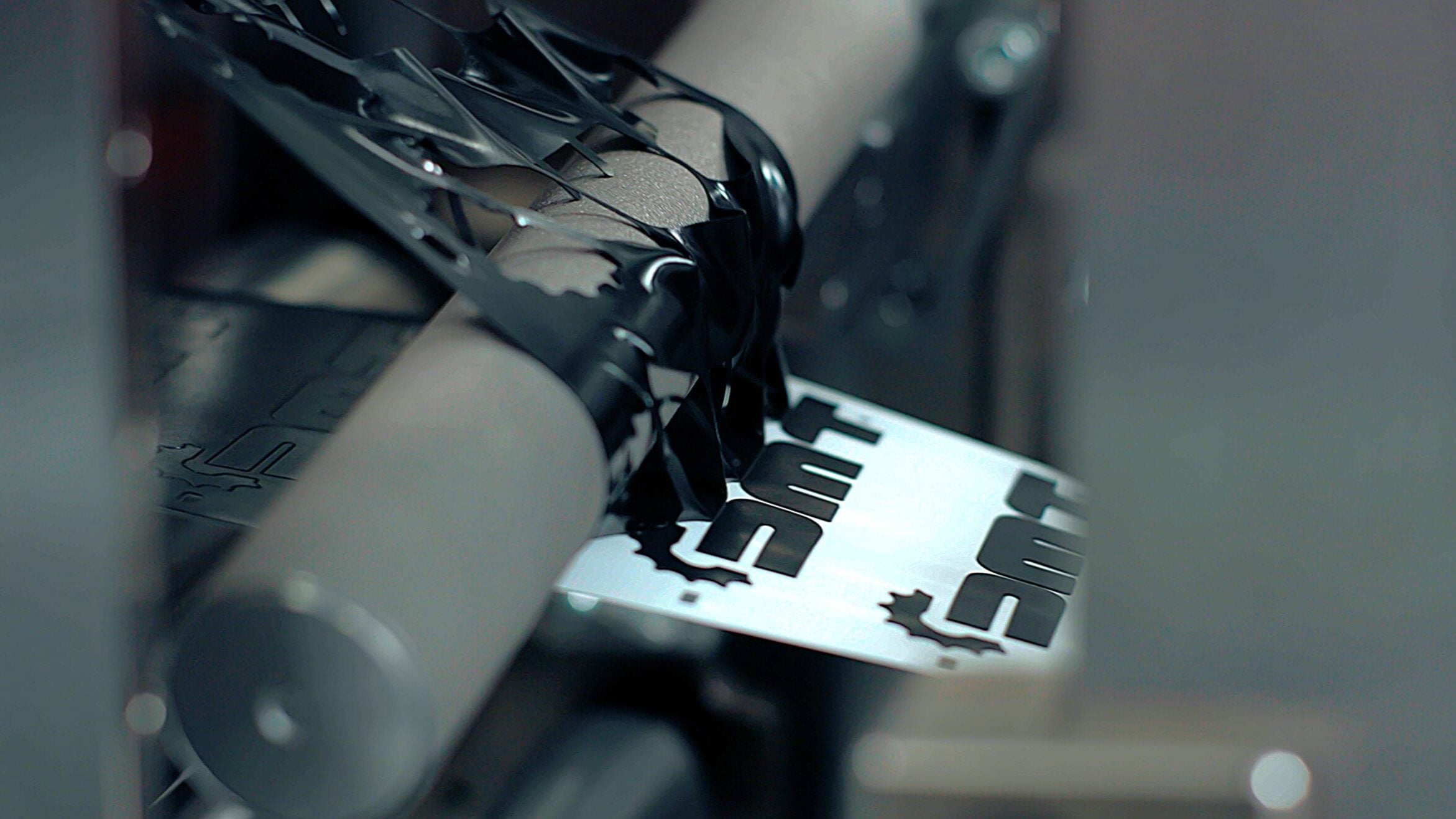 Black lettering being applied to a white surface by a machine with rollers.