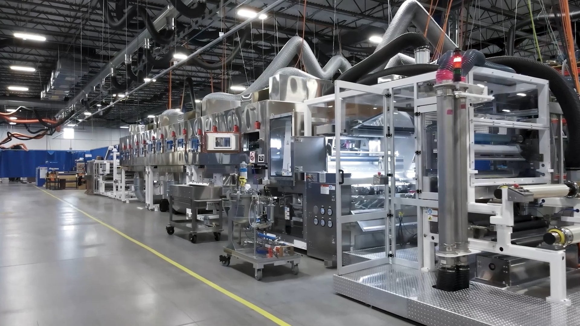Industrial manufacturing line with automated machinery and overhead ventilation systems.