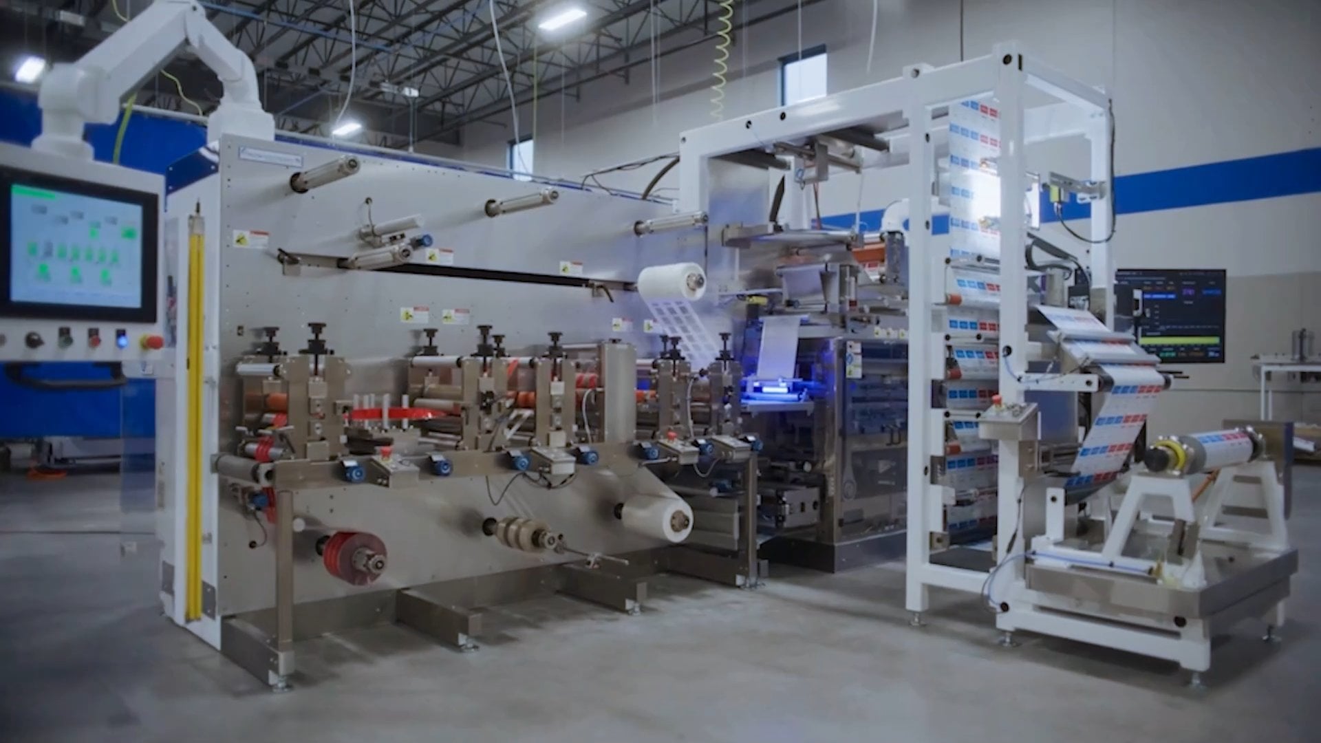Industrial packaging machine with touchscreen control and rolls of printed film.